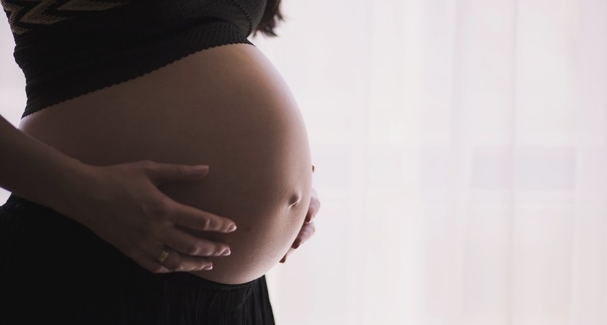 Pregnant woman holding her large, unclothed belly: guide to reduce spider veins.