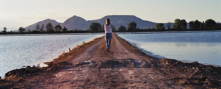A woman walking across a path that goes across a river. She's thinking about her vein problems.