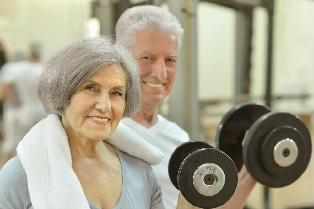 Elderly couple lifting weights at the gym to exercise to reduce leg vein pain.