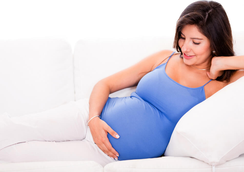 A woman laying on a couch with a hand on her pregnant belly: preventing varicose veins.