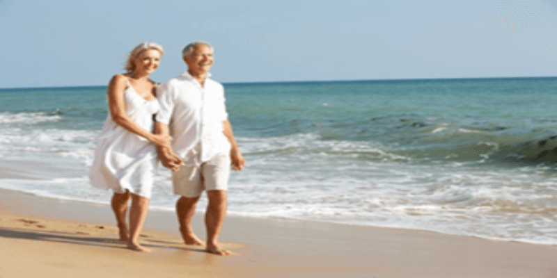Elderly couple walking on the beach with healthy legs after getting vein treatment.