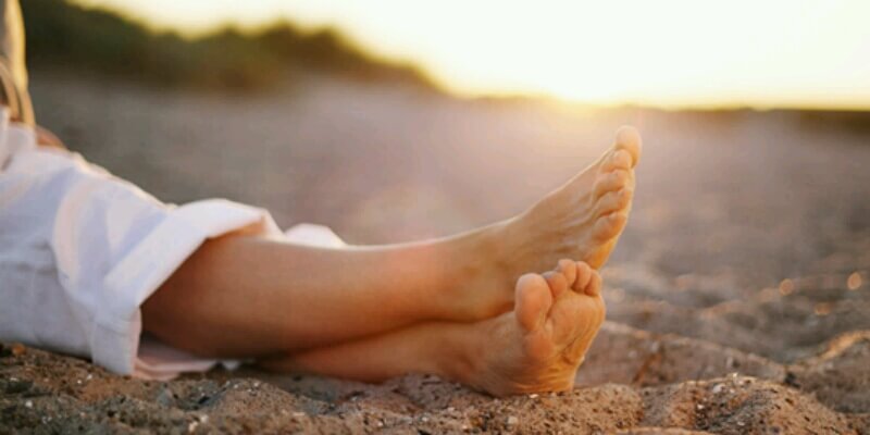 A woman's varicose vein-free legs on a sandy beach at sunset.