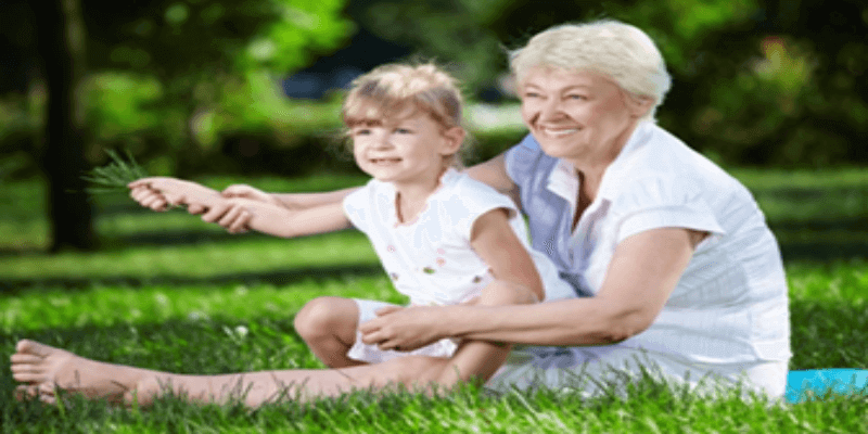Elderly woman sitting on grass outside with a child on her lap, happy she got varicose vein treatment.