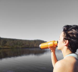 person drinking from a water bottle near a lake