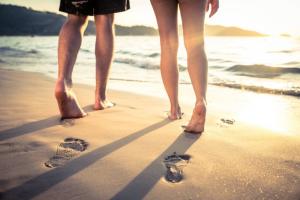 couple walking barefoot in the sand by the water