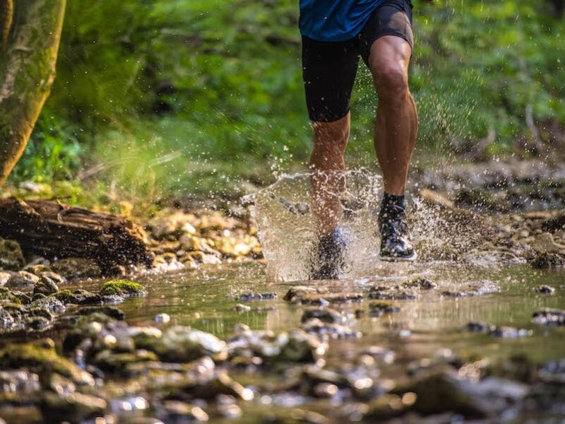 man running through the woods over a stream