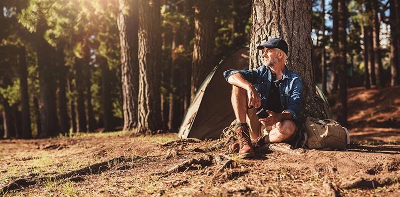 man sitting next to a tree camping