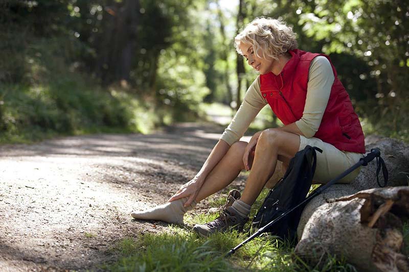 woman sitting on rock holding her ankle